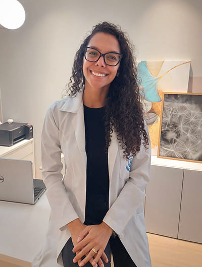 Jassanara Taveira no consultório de jaleco branco em frente a mesa